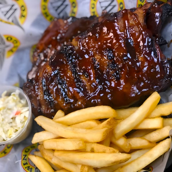 Wings To Go ribs with barbecue sauce, a side of fries, and coleslaw in a plastic cup.