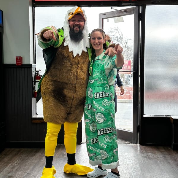 A man in an eagle costume and a woman in Eagles overalls point at the viewer.