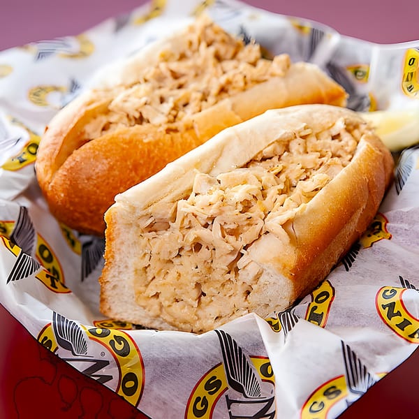 Two chicken cheesesteak sandwiches in branded Wings To Go paper, with a lemon wedge visible.