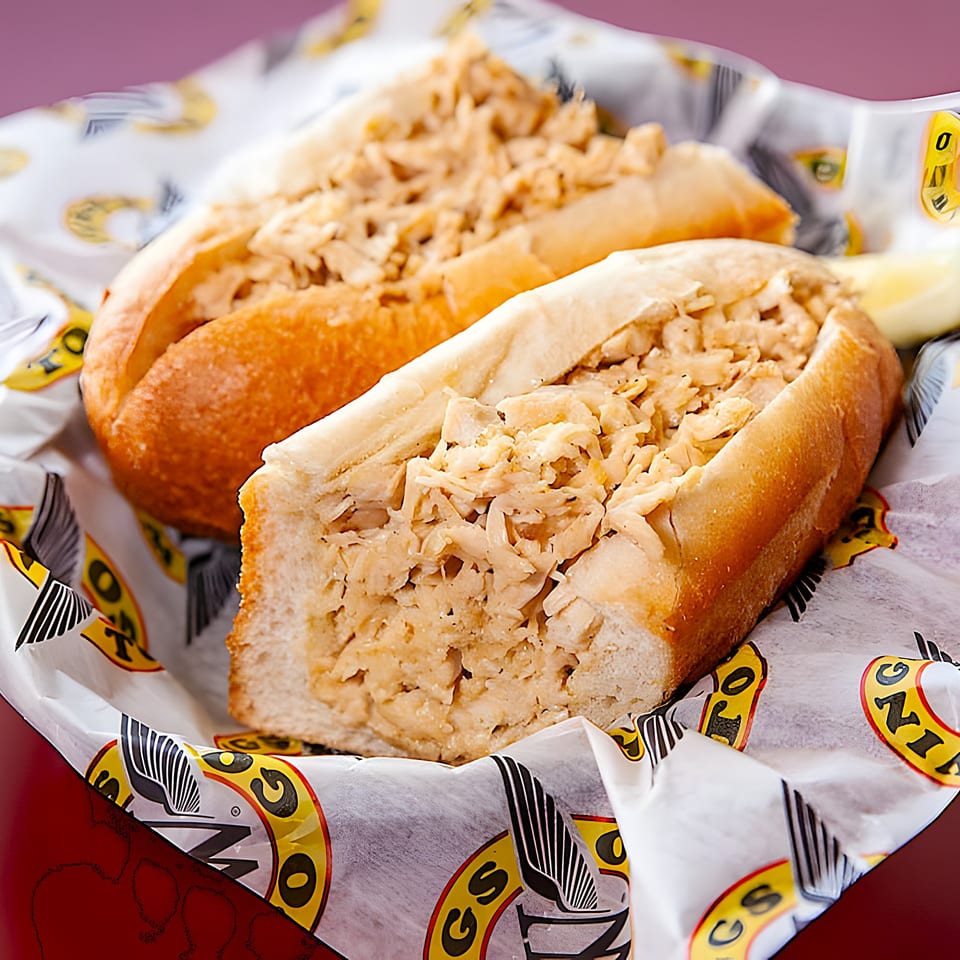 Two chicken cheesesteak sandwiches in branded Wings To Go paper, with a lemon wedge visible.