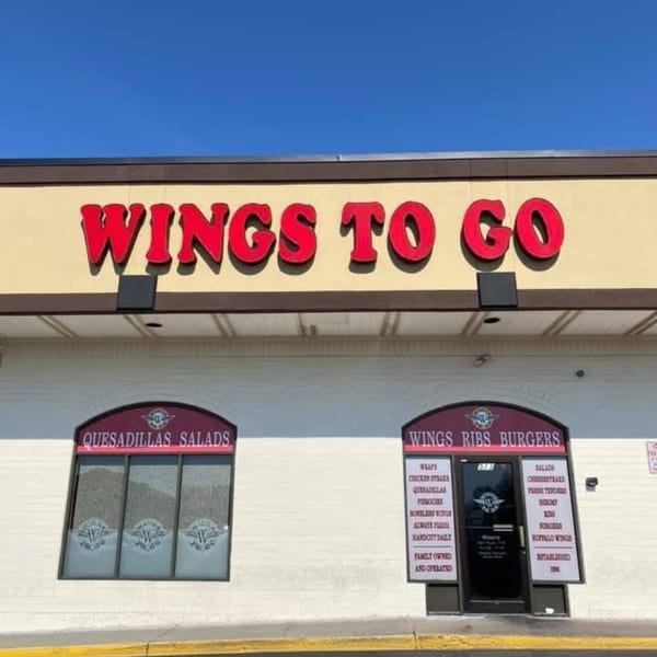 Exterior of Wings To Go restaurant with red signage, windows advertising quesadillas, salads, wings, ribs, and burgers.