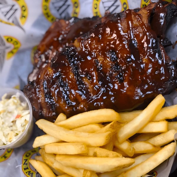 Wings To Go BBQ wings with a side of golden fries and coleslaw in a basket.
