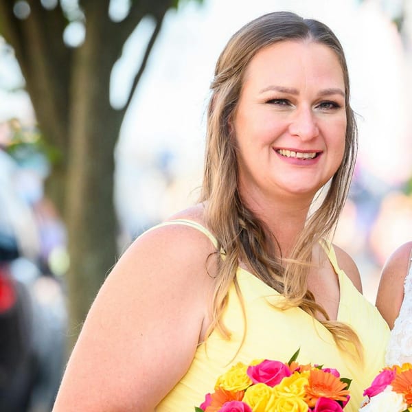 Smiling woman in a yellow dress holding a bouquet of colorful flowers.
