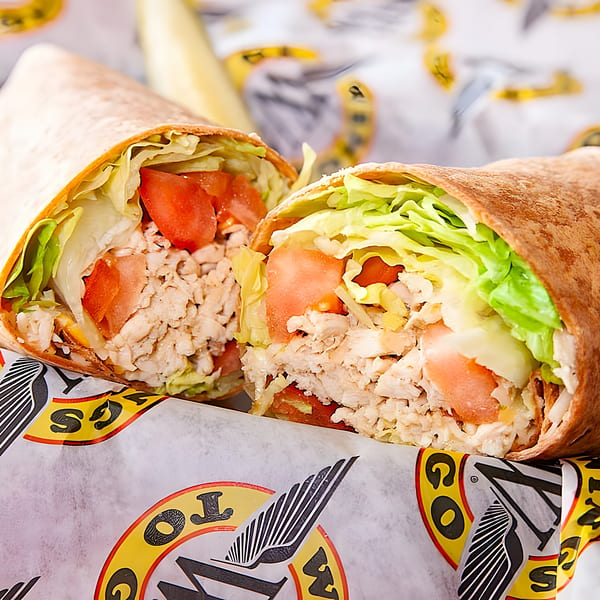 A chicken wrap, cut in half, filled with chicken, lettuce, and tomatoes, in Wings To Go branded paper.