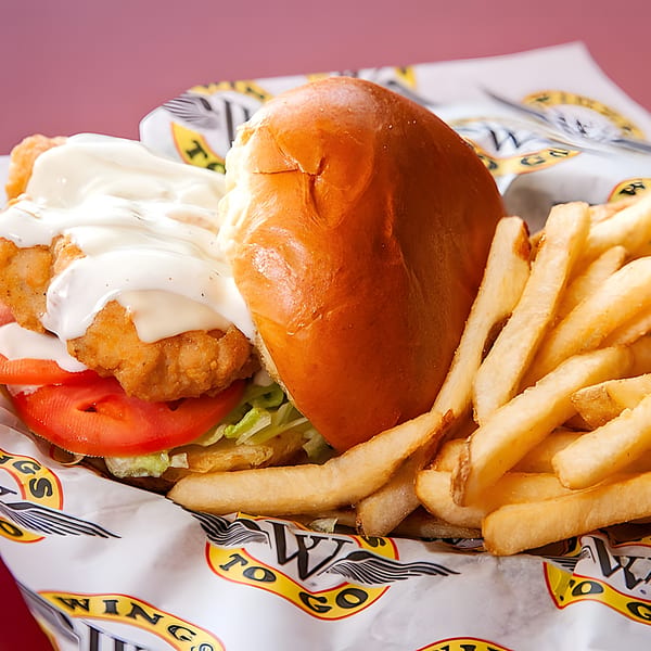 Wings To Go fried chicken sandwich with lettuce, tomato, and sauce, served with fries.