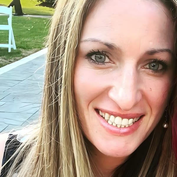 Smiling woman with long blonde hair and blue eyes, with a green lawn in the background.